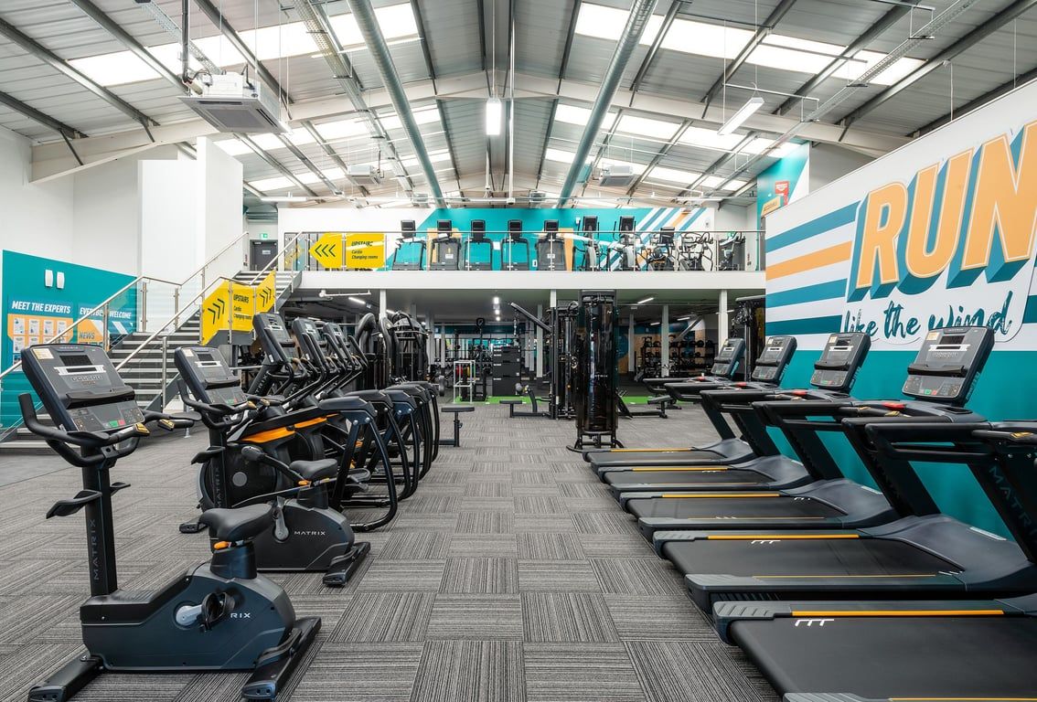 PureGym Cannock Orbital Retail Park: Rows of treadmills, ellipticals, and weight machines in a brightly lit fitness studio.