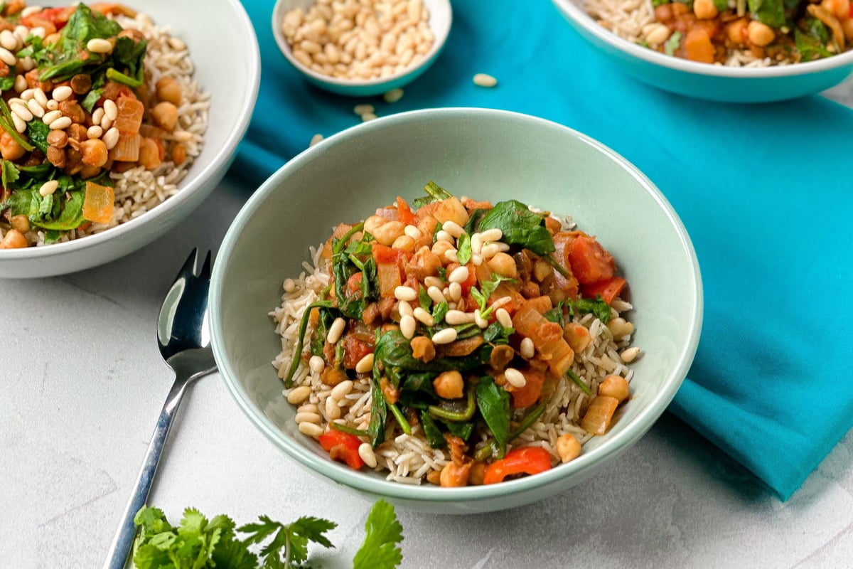 Bowls of rice topped with chickpea and lentil curry with spinach and pine nuts