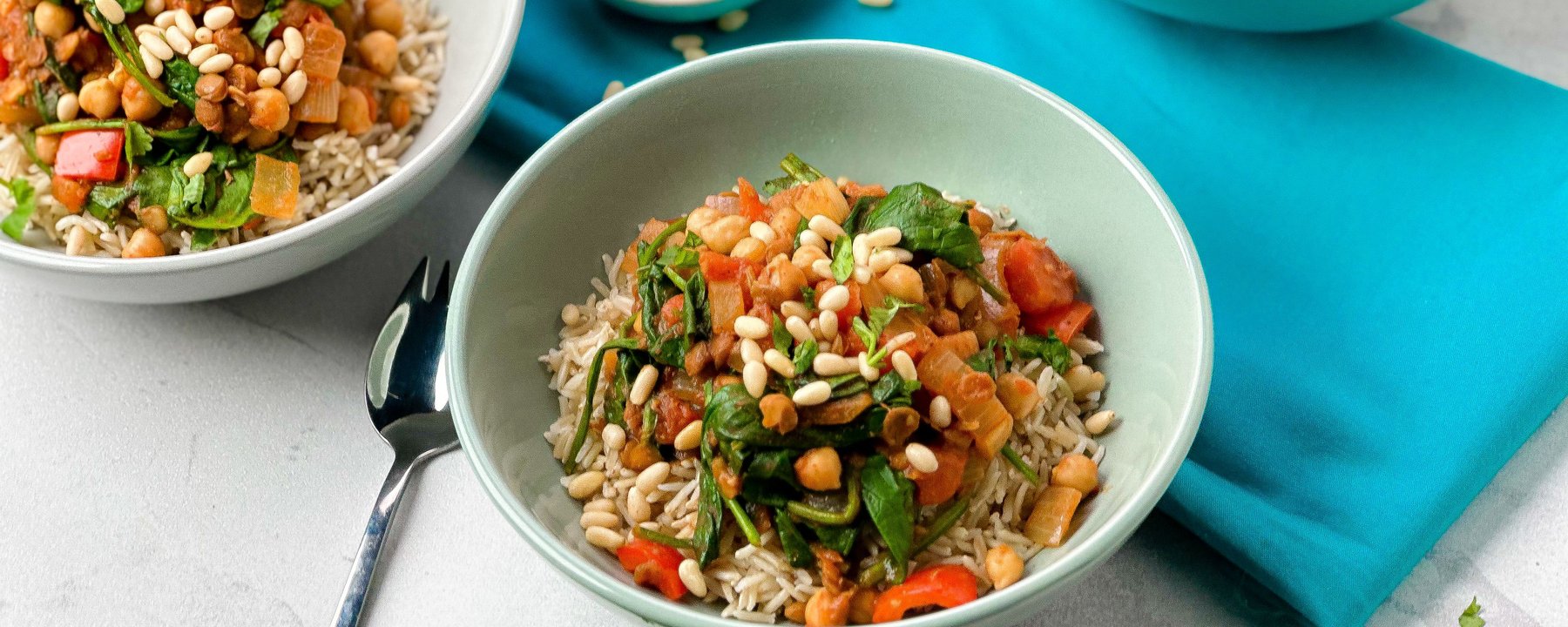 Bowls of rice topped with chickpea and lentil curry with spinach and pine nuts