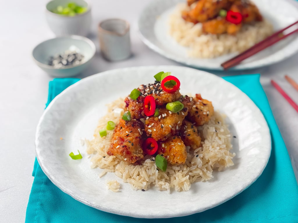 Crispy chicken pieces on rice garnished with red chili slices, spring onions, and sesame