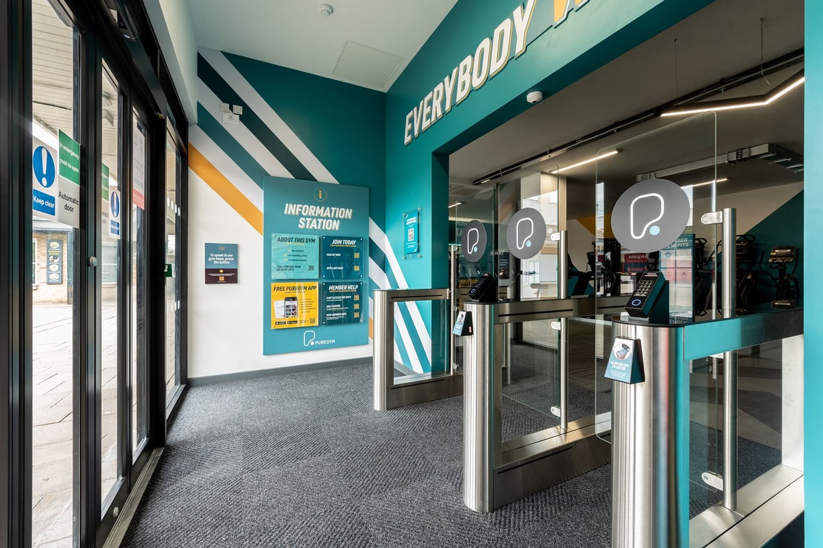 PureGym Coalville: Information desk, turnstiles, and waiting area of what appears to be a gym or fitness facility entrance.
