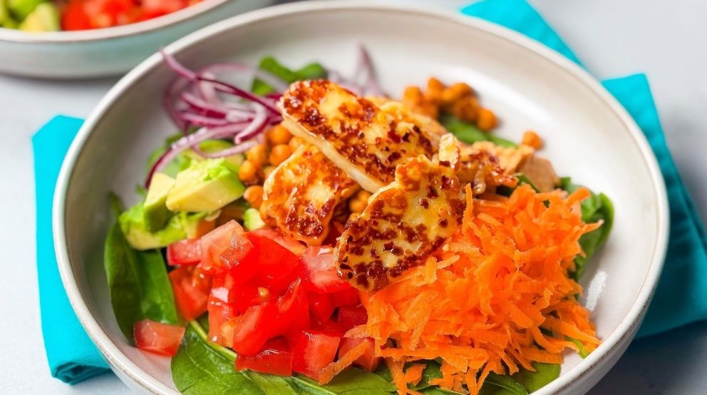Salad with grilled halloumi, shredded carrot, diced tomato, avocado, spinach, and red onion