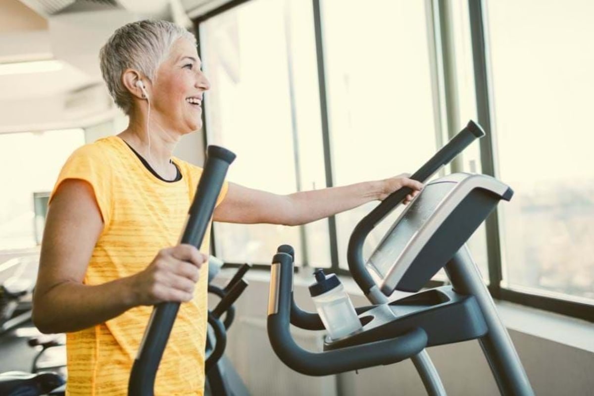Woman in yellow top exercising on elliptical machine near large windows