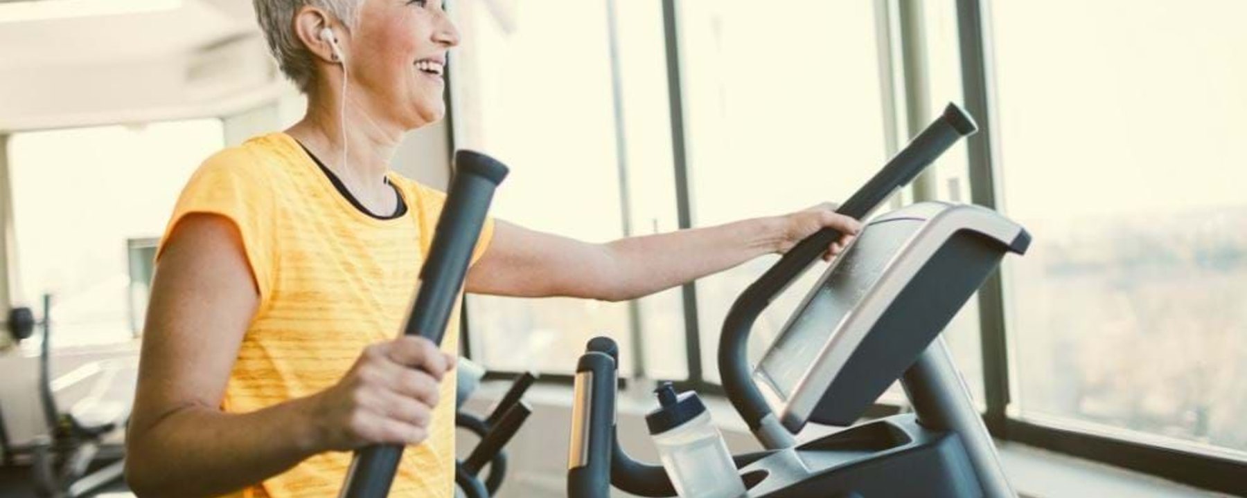 Woman in yellow top exercising on elliptical machine near large windows