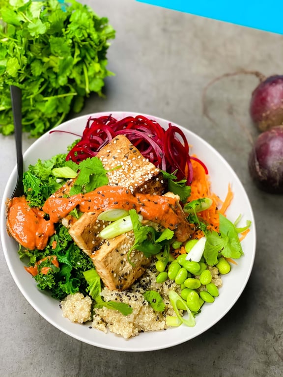 Bowl with tofu, quinoa, kale, edamame, shredded carrot, beet spirals, and sauce