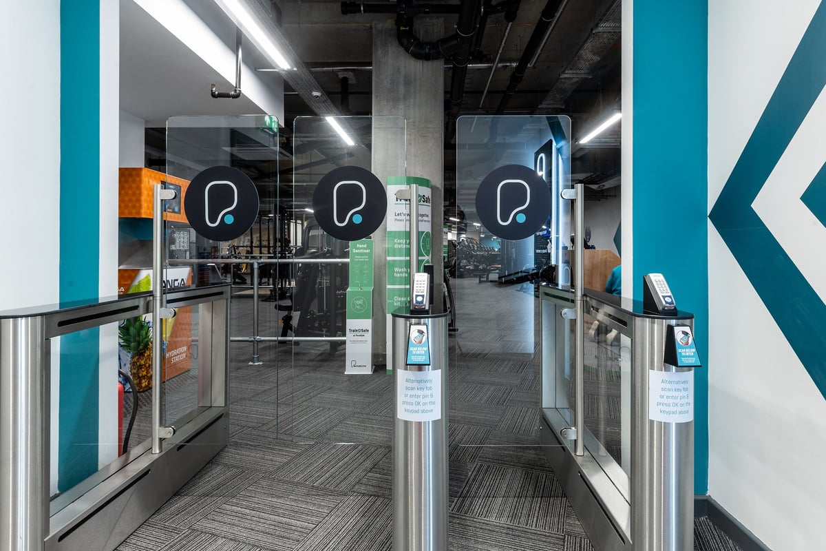 PureGym London Hoxton: Turnstiles for entrance access, self-service kiosks, and a corridor-like space.