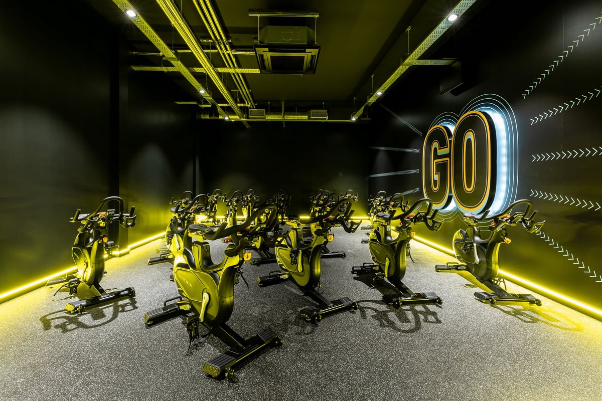 PureGym Maidenhead: Yellow-tinted exercise bikes with illuminated "GO" signage in a dimly lit studio setting.
