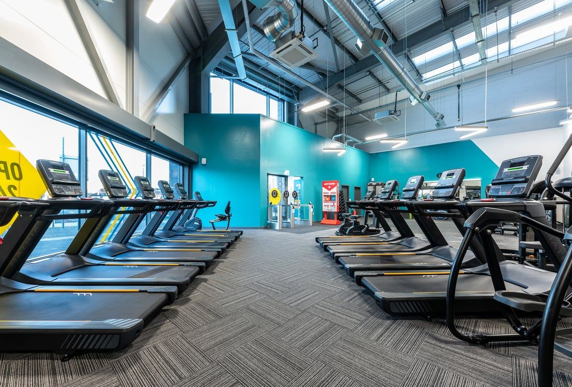 PureGym Kirkby: Rows of treadmills and exercise machines in a bright blue-walled gym interior.