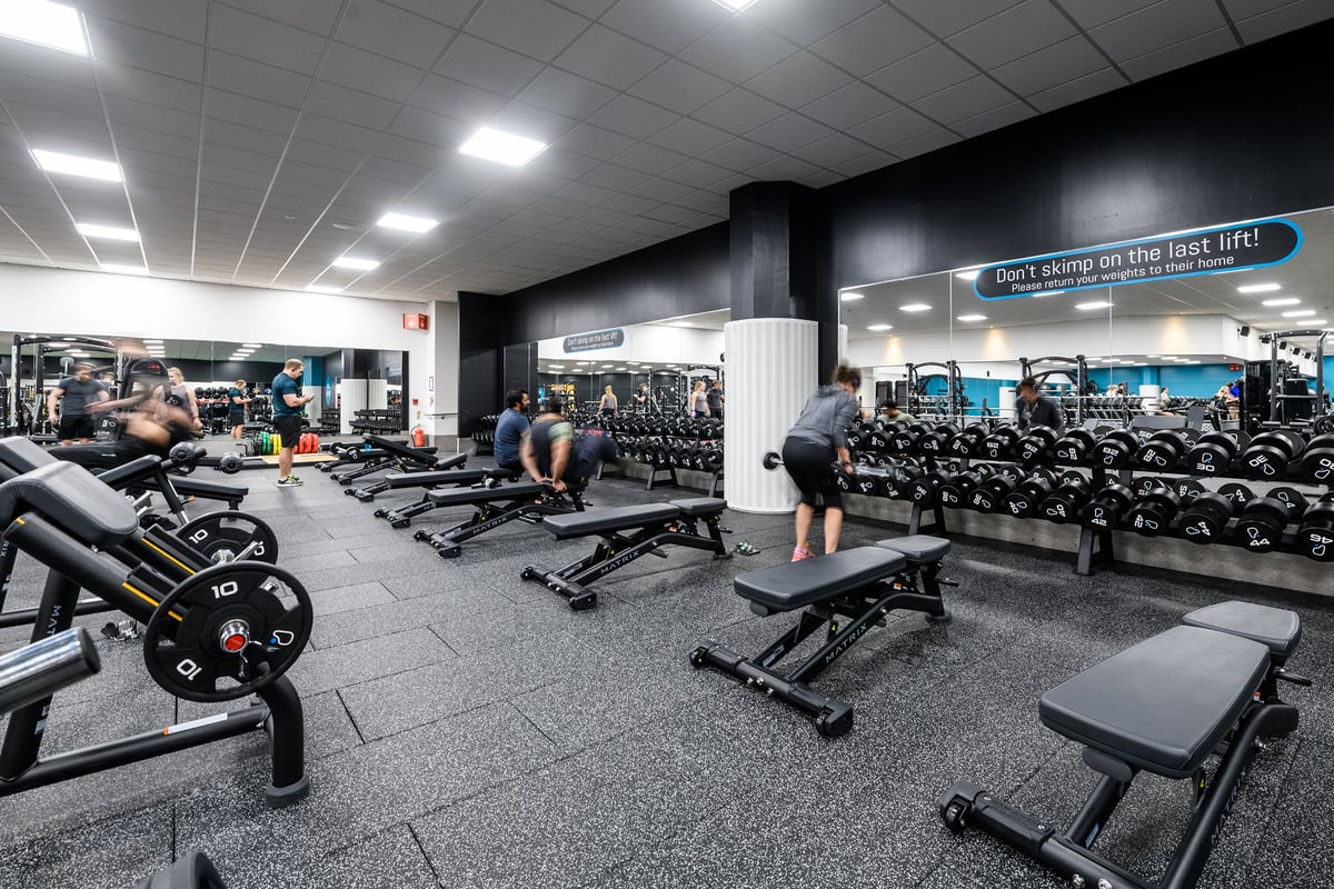 PureGym Aylesbury: Weight benches, free weights, resistance machines, and dumbbell racks in a dimly lit gym interior.