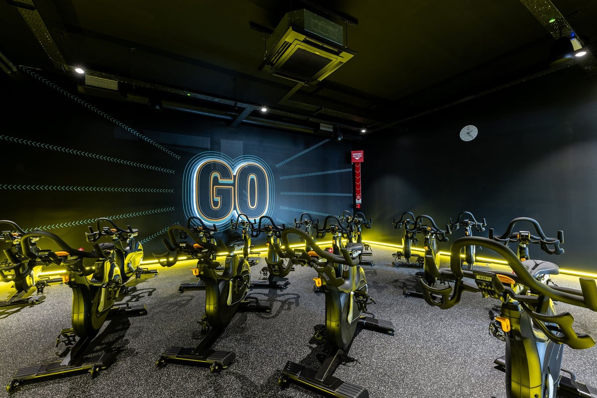 PureGym Crewe Grand Junction Retail Park: Rows of yellow spin bicycles inside a dimly lit studio with neon 'GO' signage.