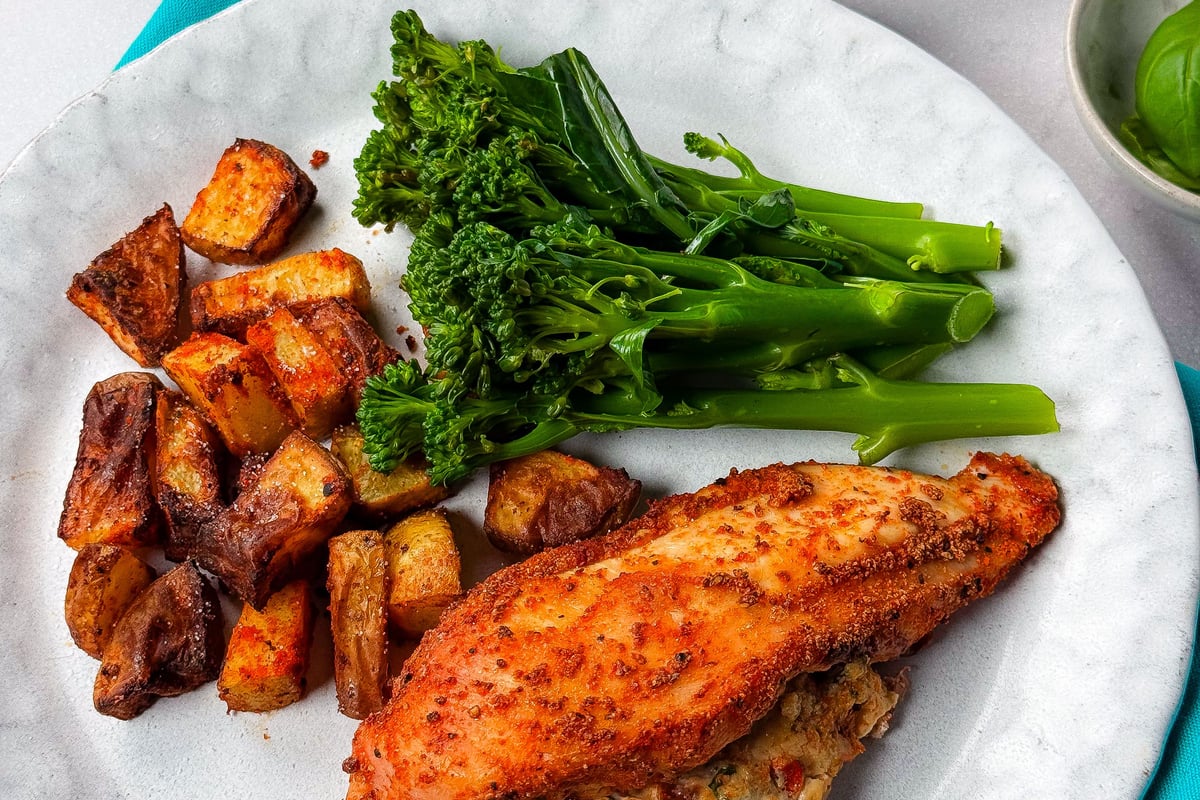 Stuffed chicken breast with roasted potatoes and steamed broccolini on a white plate