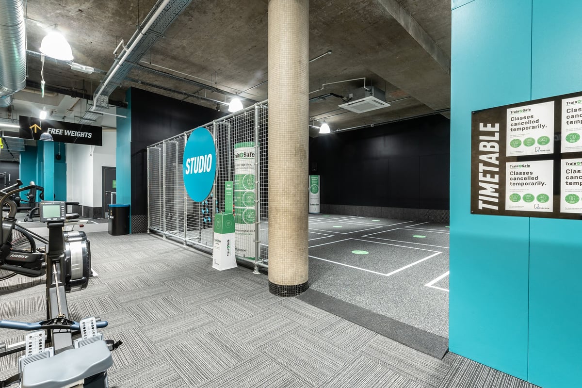 PureGym London Leytonstone: Grey treadmills, a spin studio with teal accents, exposed concrete pillars and floor markings.