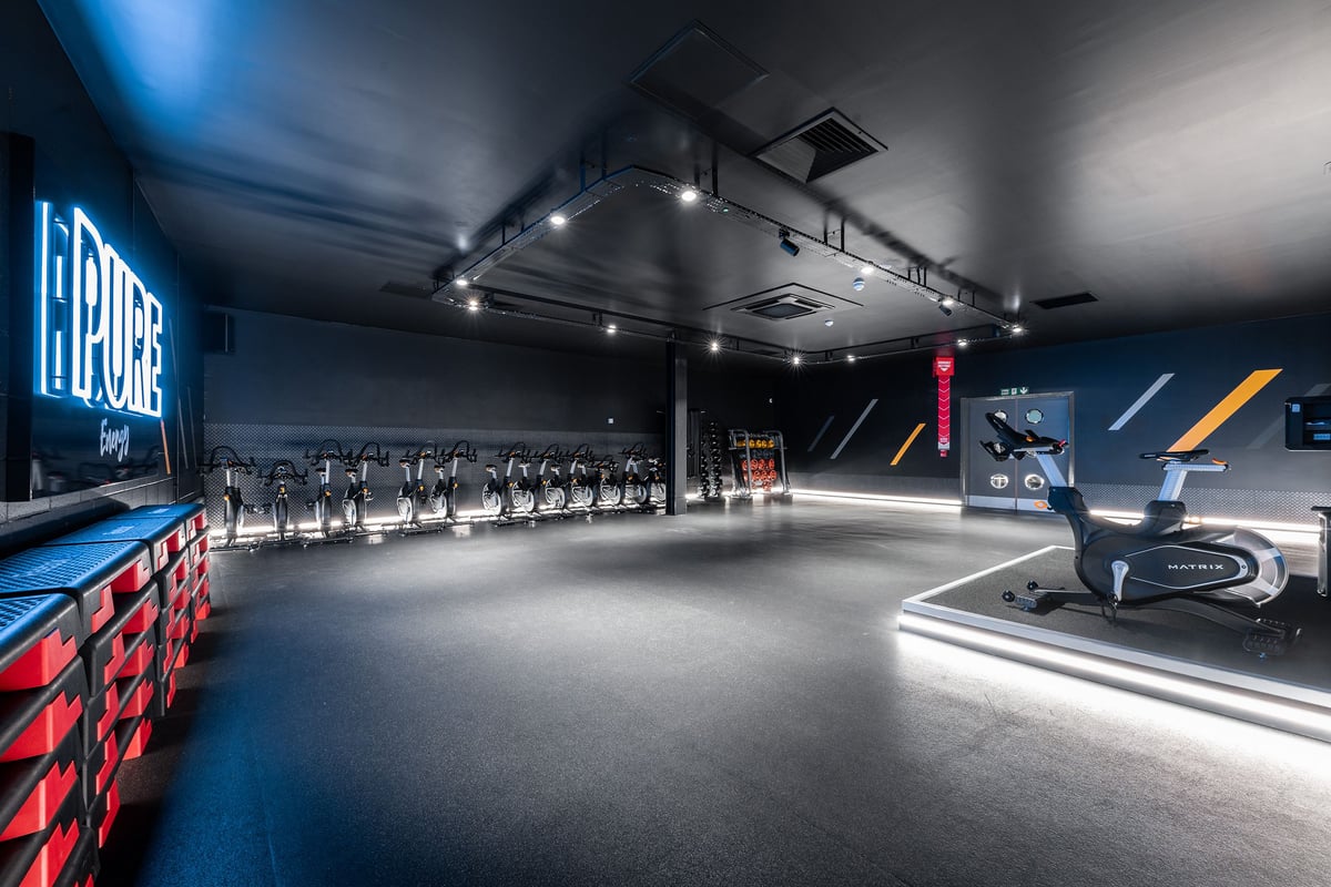 PureGym Hednesford Cannock: Rows of stationary bikes, mirrored walls, sleek black and blue colour scheme.