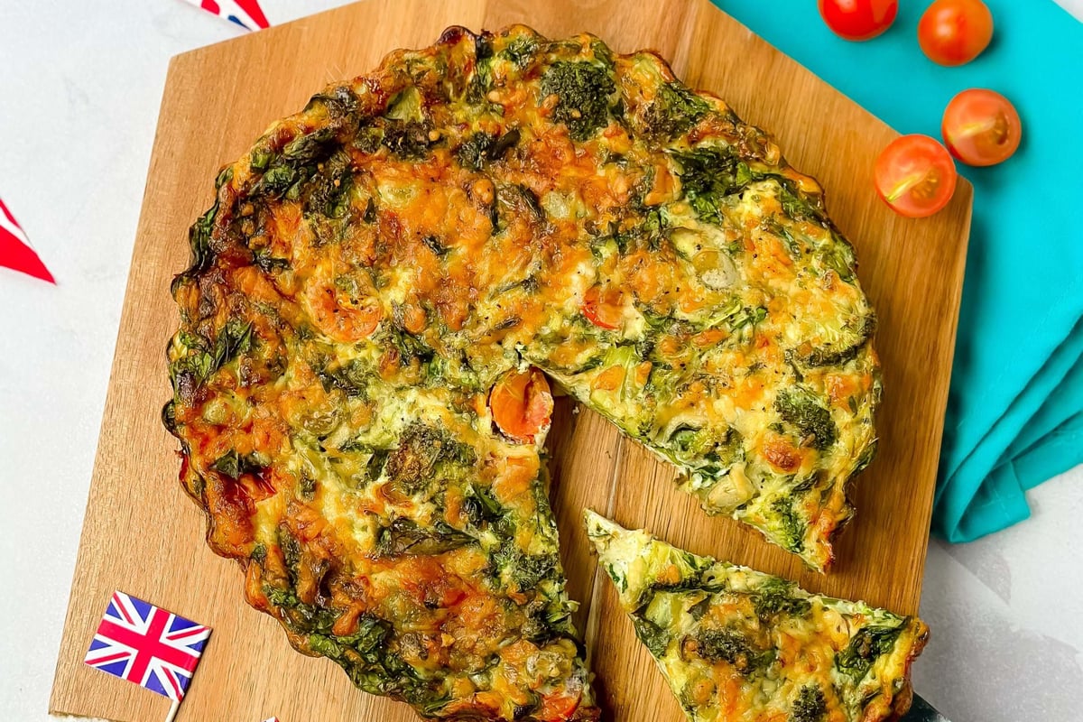 Vegetable quiche with a slice being served on a wooden board with Union Jack flags.
