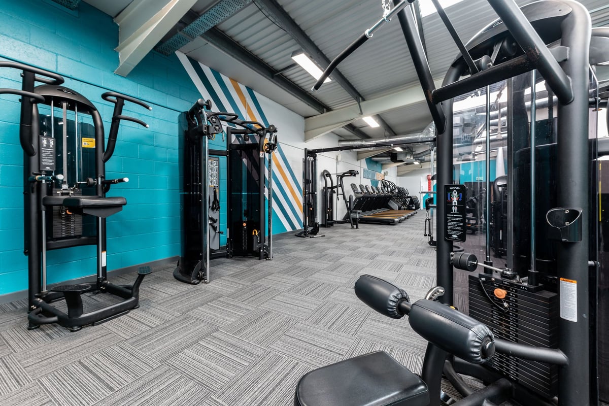 PureGym Gloucester Retail Park: Gym interior with weight machines, benches, rubberized flooring in teal and grey tones.