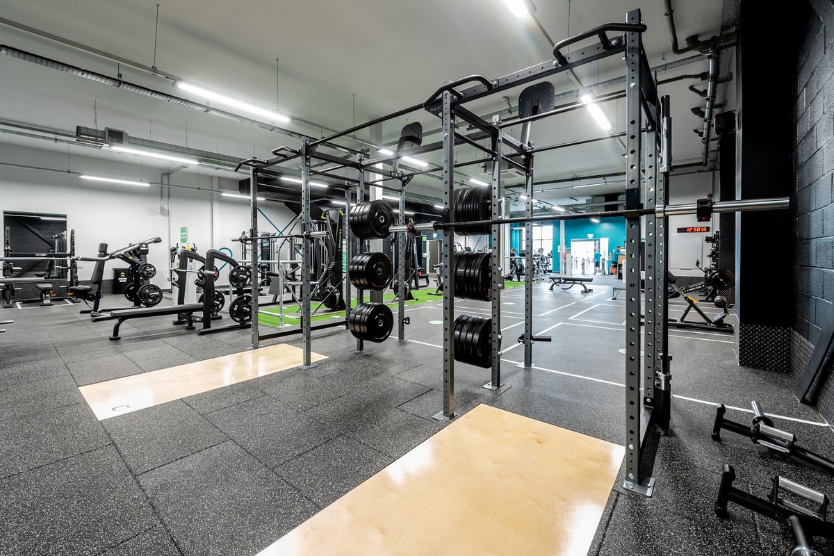 PureGym Birmingham Longbridge: Strength training area with power racks, weight plates, bars, and rubberized flooring.