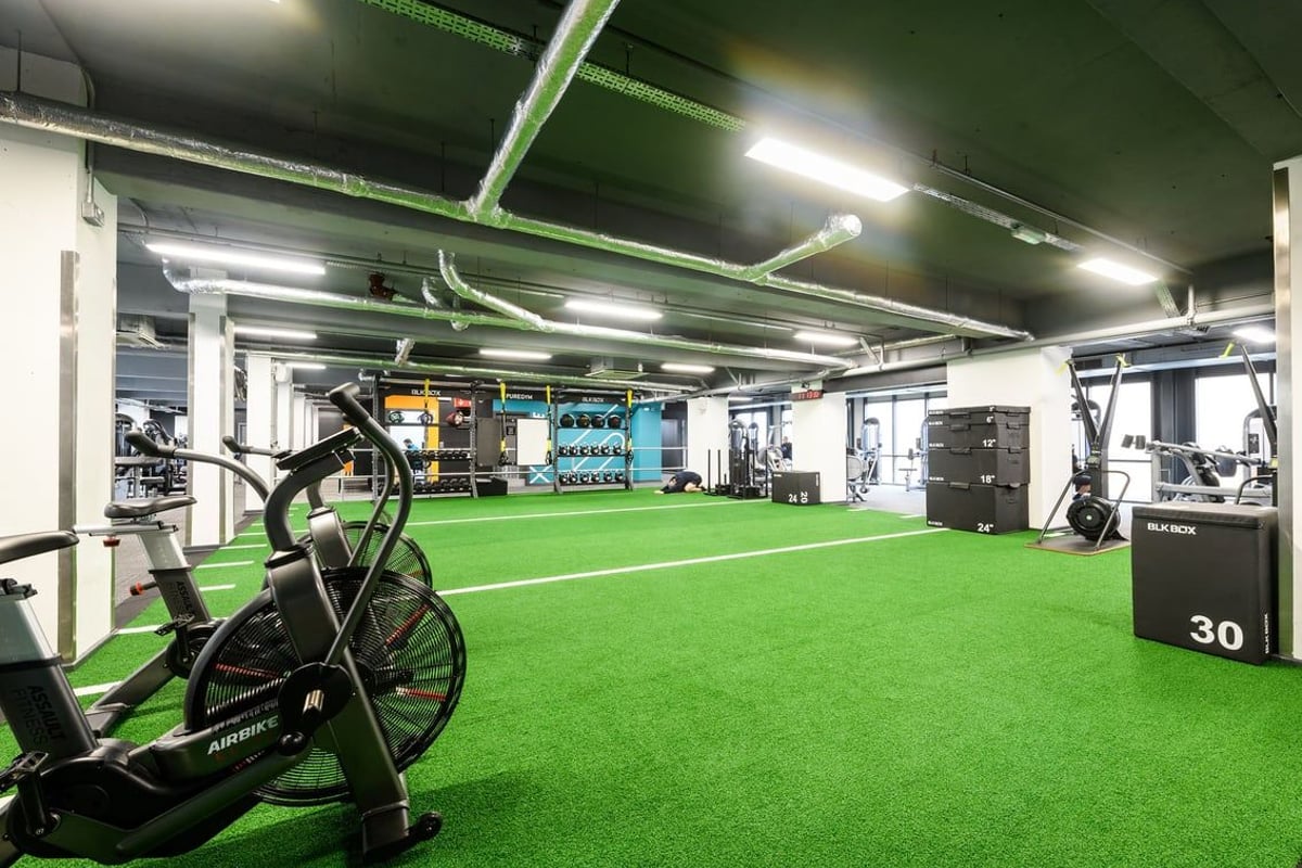 PureGym London Lambeth: Indoor turf area with exercise bikes, weights, and neon green accents.