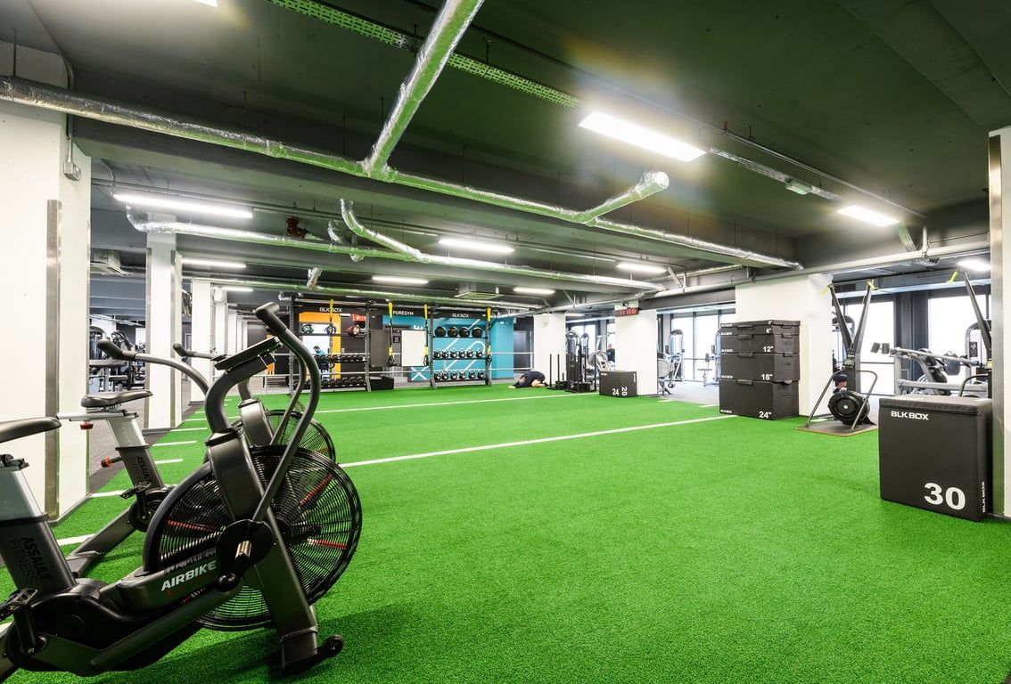 PureGym London Lambeth: Indoor turf area with exercise bikes, weights, and neon green accents.