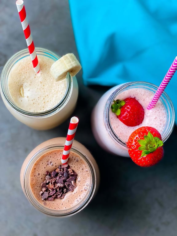 Three smoothies in jars with striped straws, topped with banana slice, strawberries