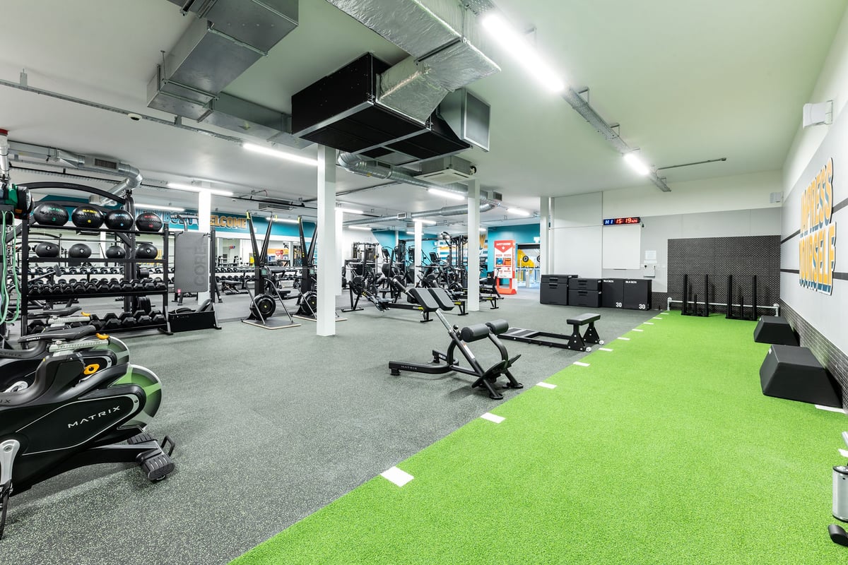 PureGym Boston: Weightlifting racks, free weights, turf area, exercise machines, mirrored walls in a modern gym facility.