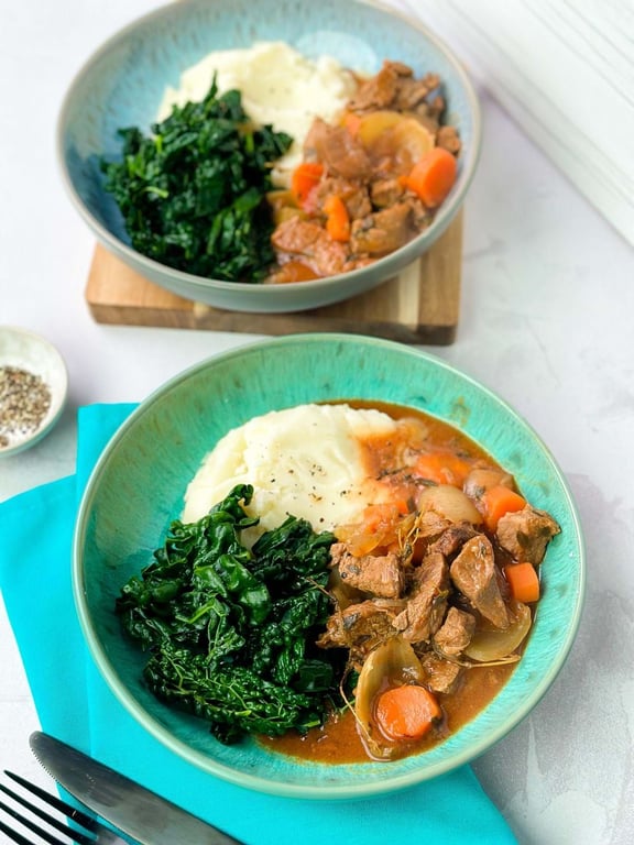 Mashed potatoes, cooked kale, and beef stew with carrots and onions in bowls