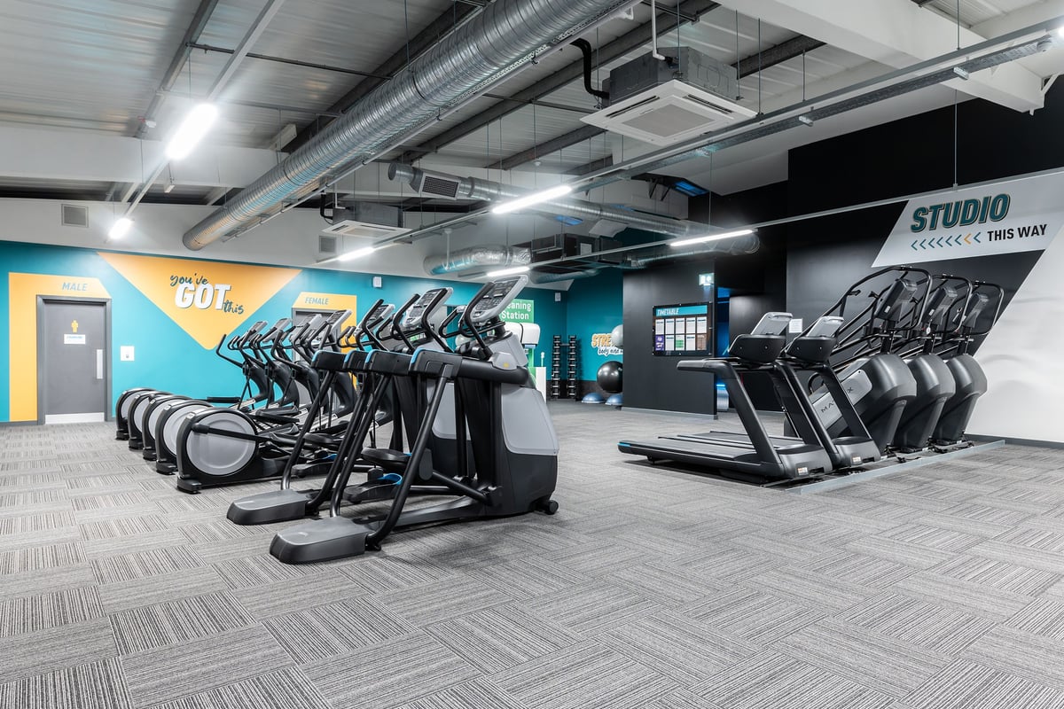 PureGym Torquay Bridge Retail Park: Rows of exercise bikes and treadmills in a studio with teal accents and mirrored walls.