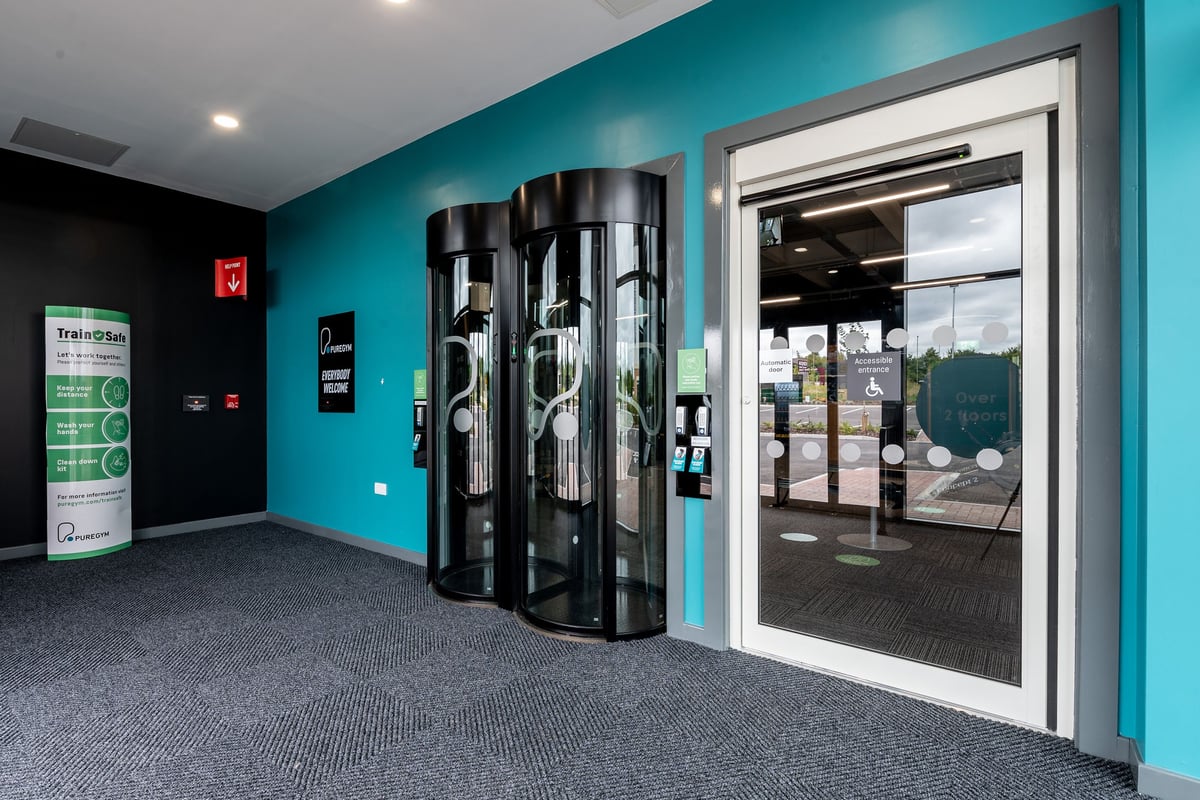 PureGym Andover: Revolving security turnstiles at gym entrance, turquoise walls, and floor mat.
