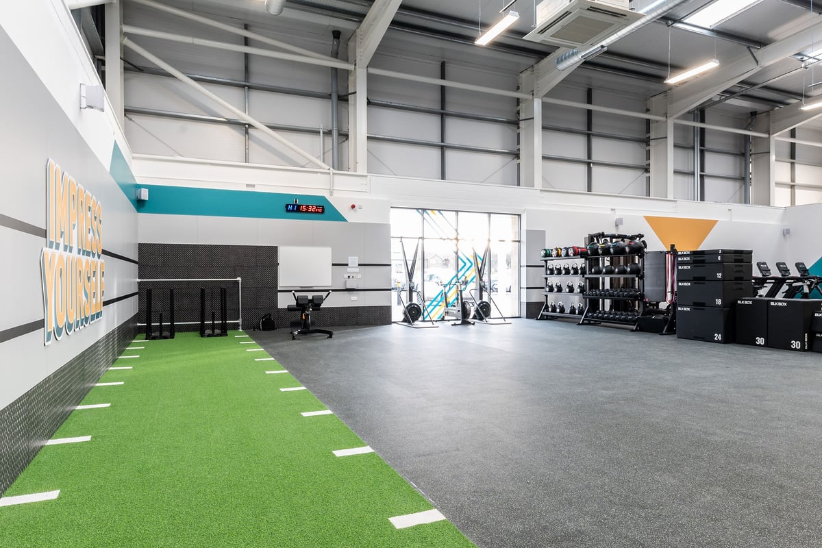 PureGym Blyth: Rows of exercise rigs, green turf area, weight racks, and mirrored walls.