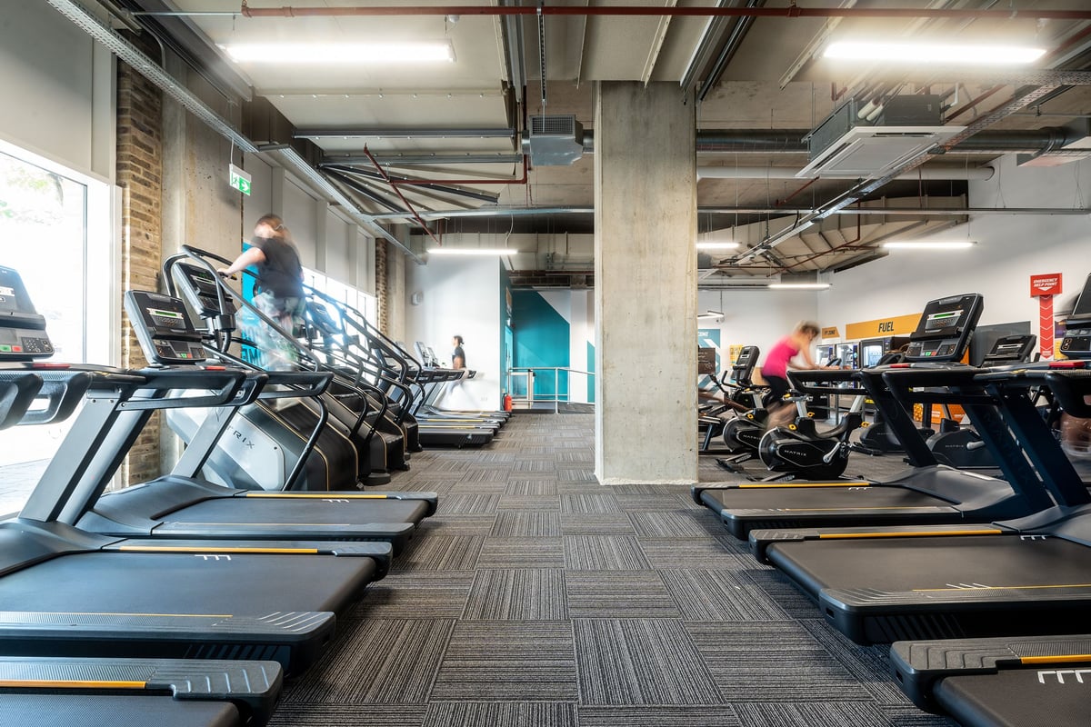 PureGym London Woolwich: Rows of treadmills, cross trainers, exposed ceiling utilities in an industrial-style gym interior.