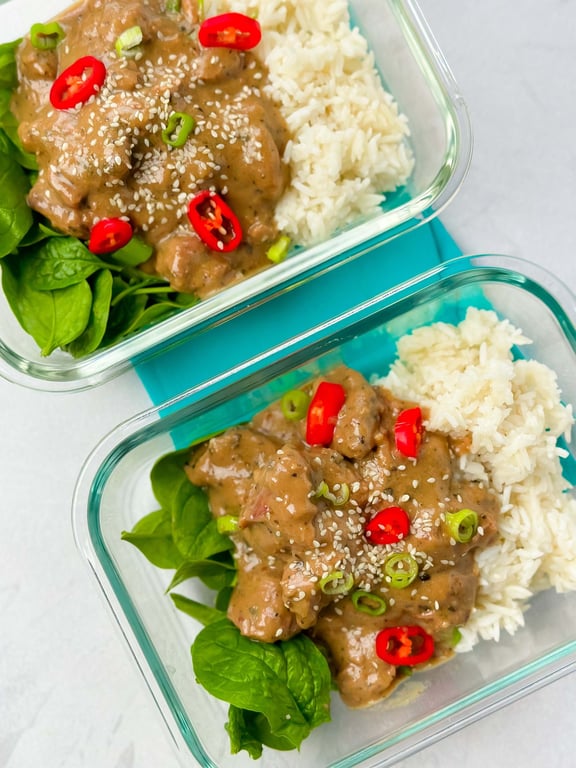 Two glass containers with rice, spinach, creamy sauce, red chili, spring onion, and sesame