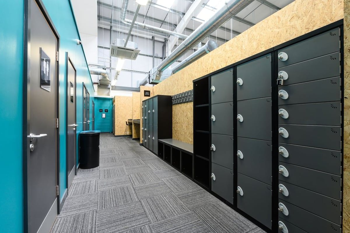 PureGym Saffron Walden: Rows of lockers, benches along the corridor, and tiled flooring.