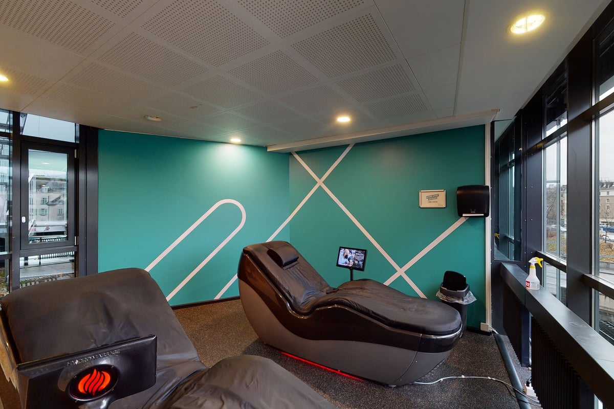 PureGym Zürich Lochergut: Fauteuils de massage, néons traversant un mur bleu sarcelle, plafond suspendu dans une salle de sport à domicile ou un studio.