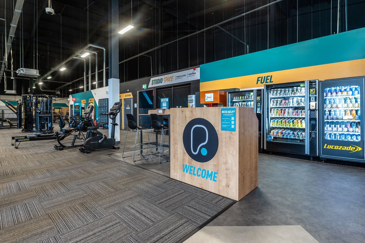PureGym Stockton-on-tees Teesside Park: Vending machines, welcome kiosk, bar stools inside a commercial space.