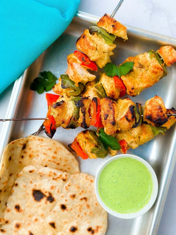Grilled chicken and vegetable skewers with flatbread and green chutney on a metal tray