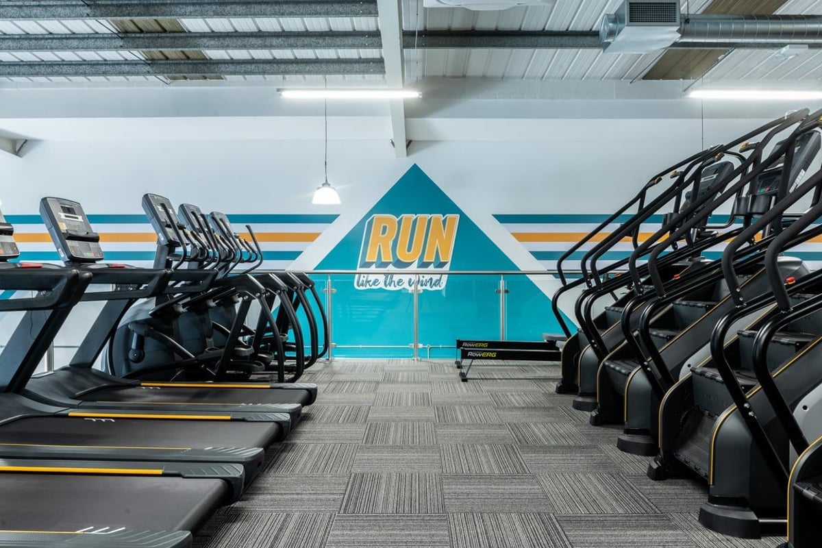PureGym Peterborough Brotherhood Retail Park: Rows of treadmills facing a wall with "RUN" displayed in large teal letters.