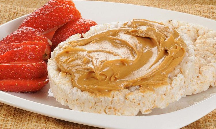 Rice cakes with peanut butter and sliced strawberries on a white plate