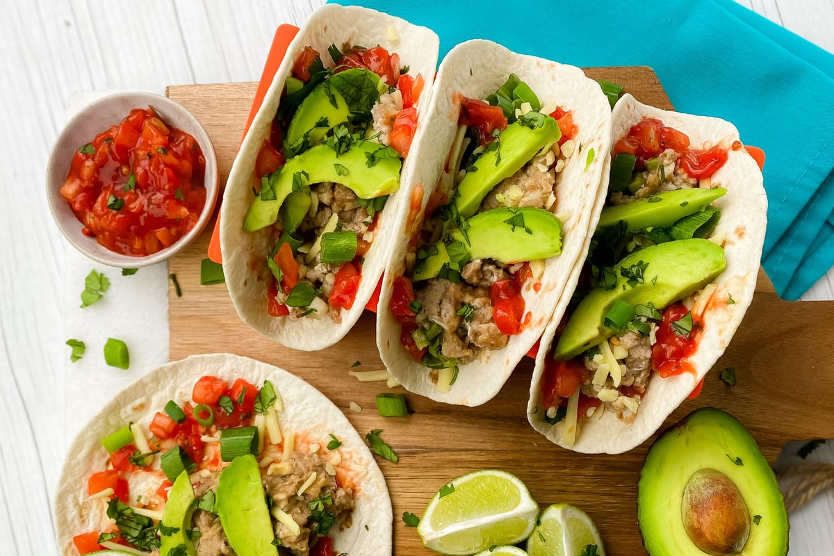 Soft tacos filled with scrambled eggs, avocado slices, salsa and herbs on wooden board