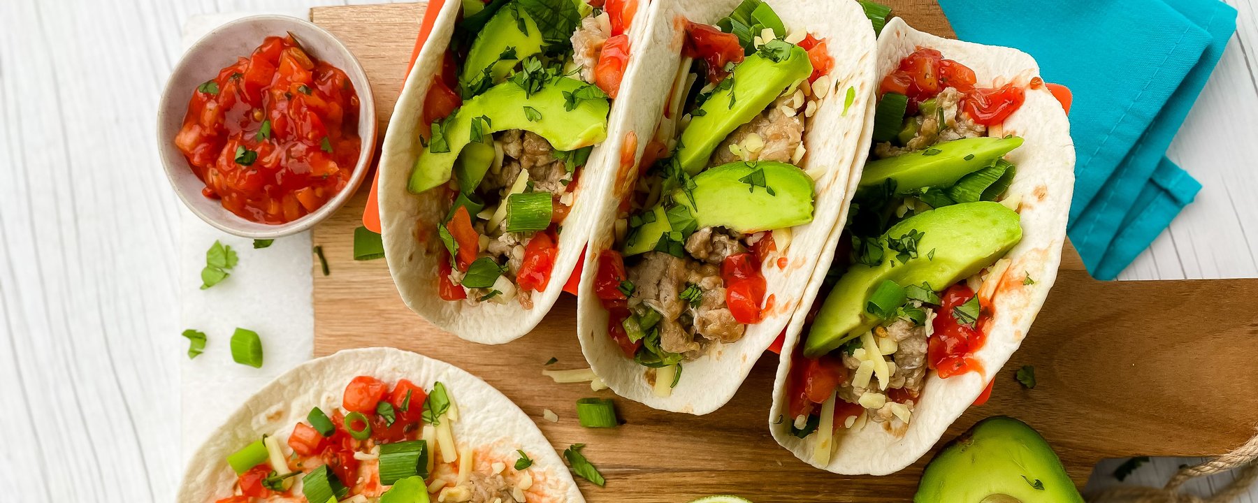 Soft tacos filled with scrambled eggs, avocado slices, salsa and herbs on wooden board