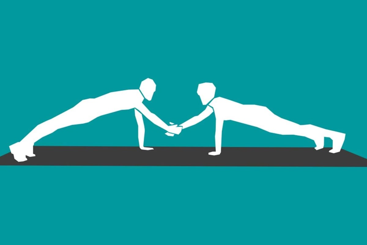 Two people doing push-ups while shaking hands on a mat against teal background