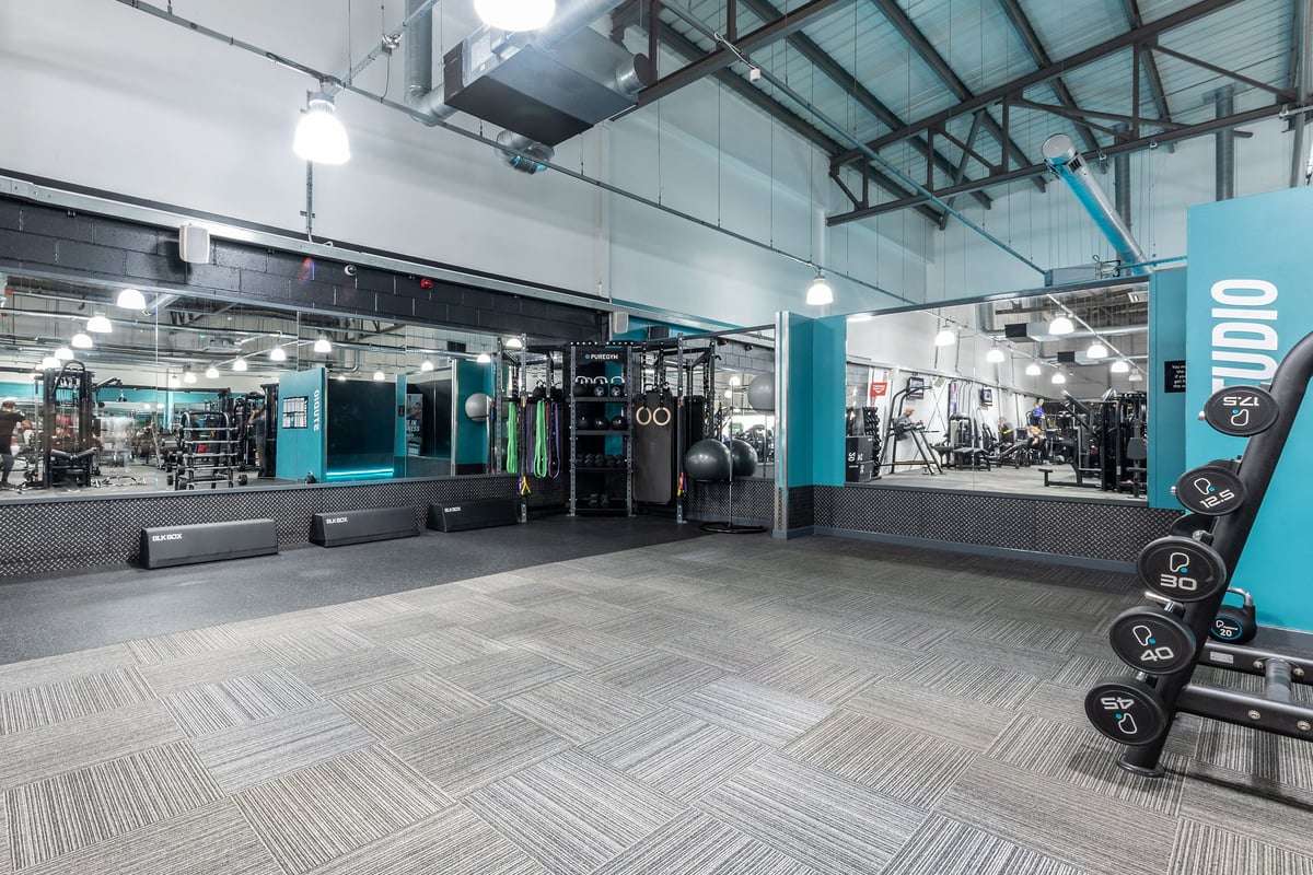 PureGym Wolverhampton Bentley Bridge: Rows of strength machines, free weights, benches, and mirrors in a bright gym studio.