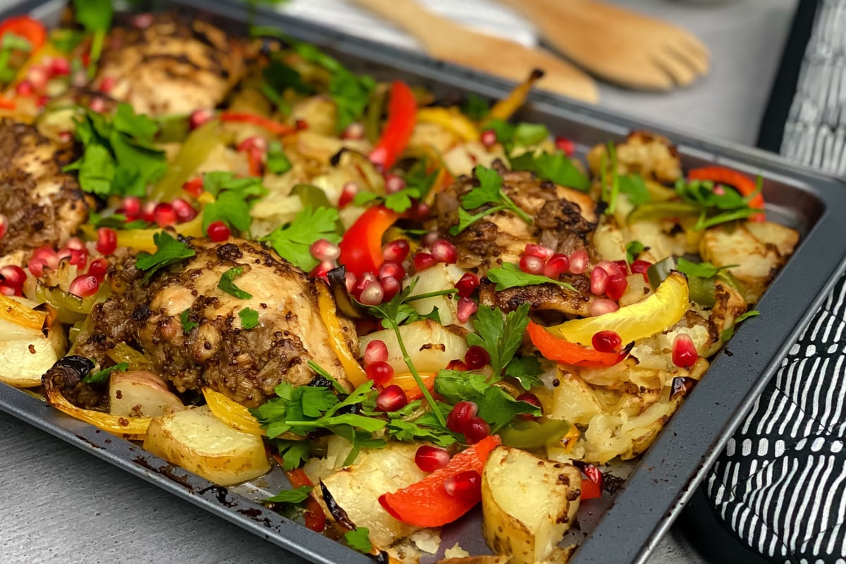 Roasted chicken thighs with potatoes, peppers and pomegranate seeds on a dark baking tray