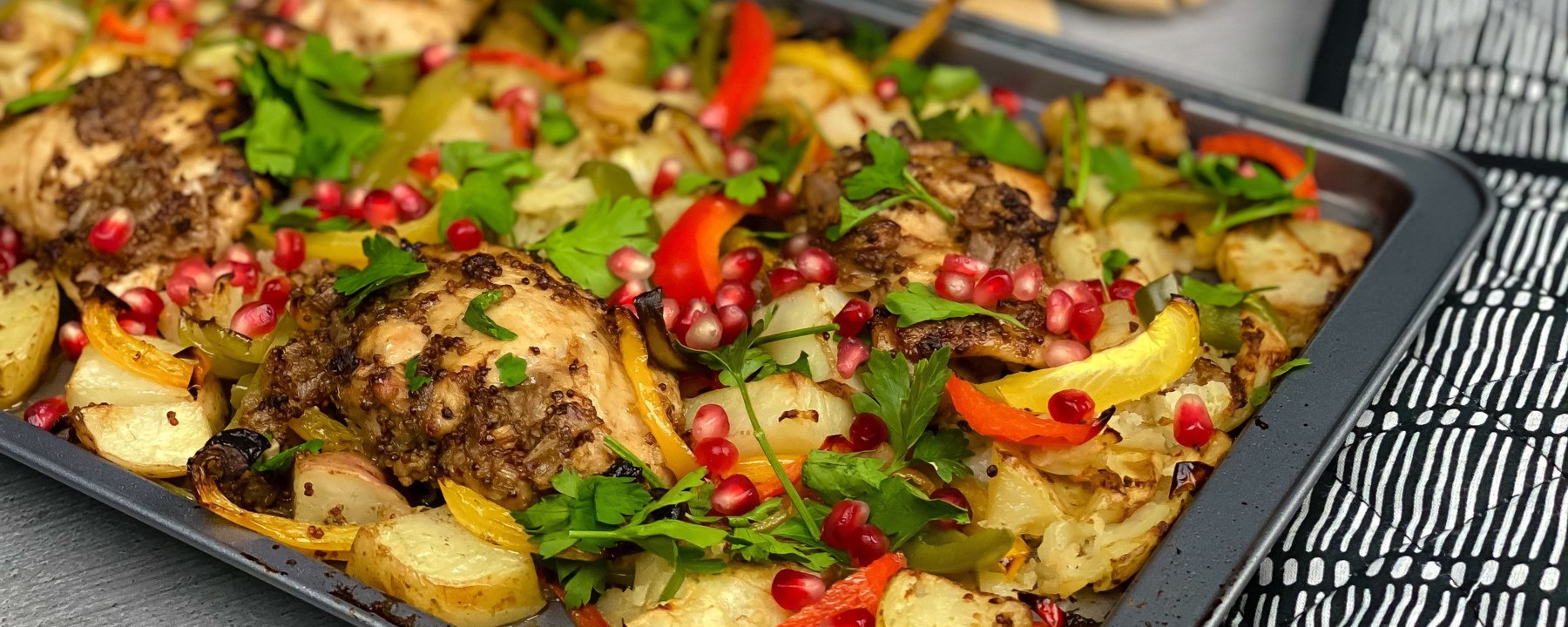 Roasted chicken thighs with potatoes, peppers and pomegranate seeds on a dark baking tray