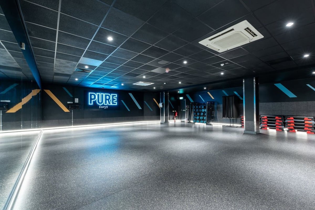 PureGym Purley: Large open space with blue-tinted lighting, mirrored walls, and rubberized flooring.