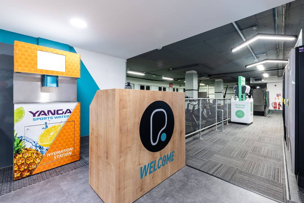 PureGym London Putney: Reception area with wooden desk, colourful branding elements, and modern industrial design.