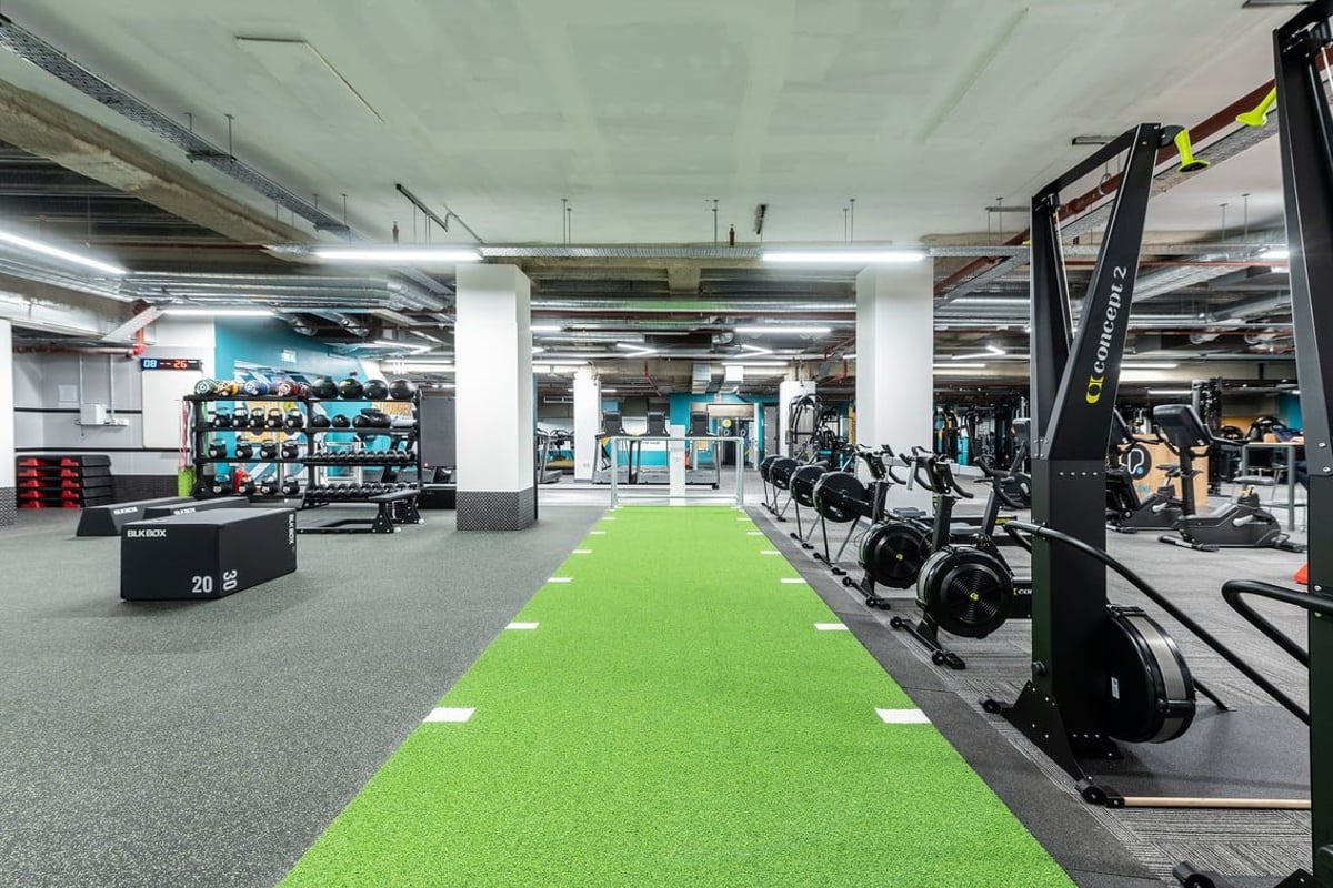 PureGym London Monument: Weightlifting area with dumbbells, resistance machines, green turf runway, and rubberized flooring.