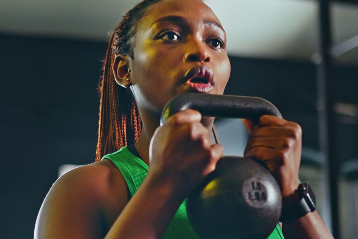 Frau in grünem Sportoberteil hält Kettlebell während des Trainings, konzentriert, Gym