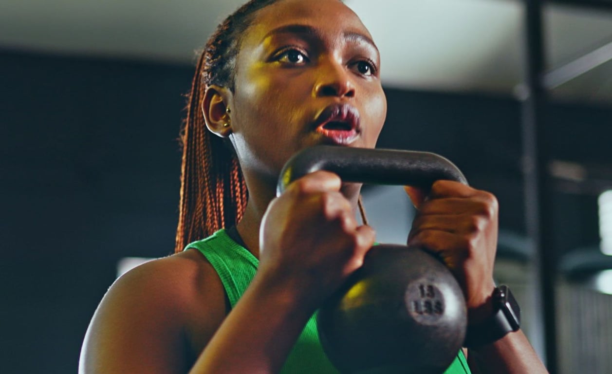 Frau im grünen Top hebt 6 kg Kettlebell im Fitnessstudio