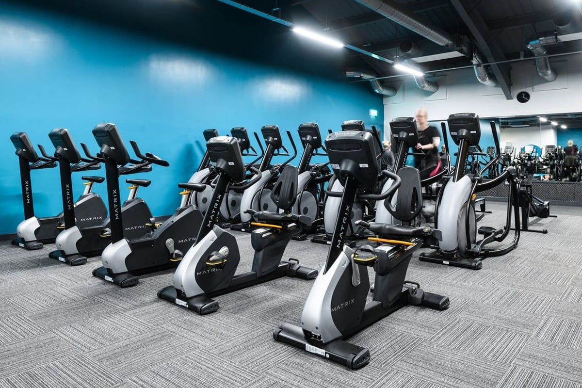 PureGym Southend Fossetts Park: Rows of stationary bikes in a dimly lit gym space with blue-tinted lighting.