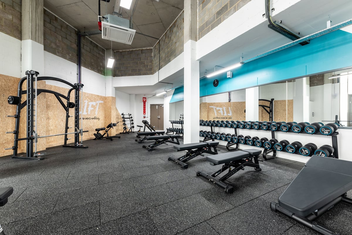 PureGym London Seven Sisters: Squat racks, dumbbell racks, weight benches, rubberized flooring in a gym weightlifting area.
