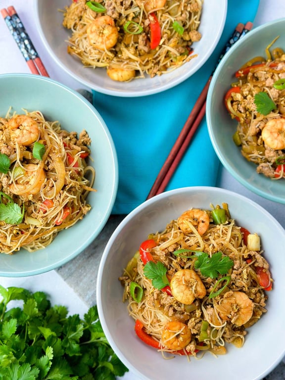 Four bowls of prawn and vegetable stir-fried noodles with chopsticks on a blue napkin